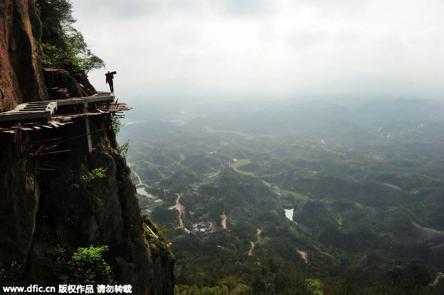 Workers balance on planks to build mountain road