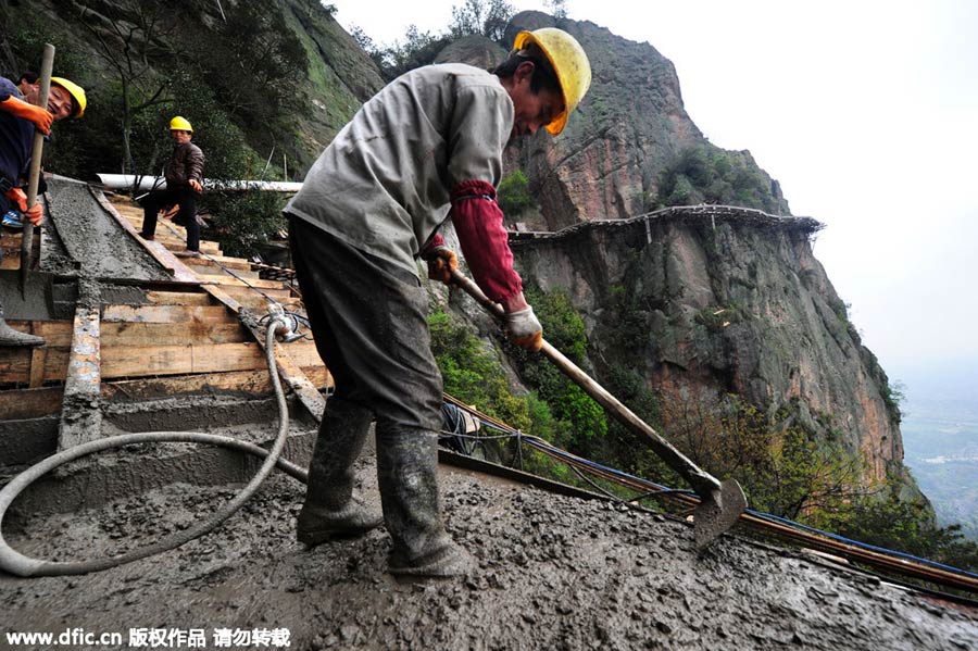 Workers balance on planks to build mountain road