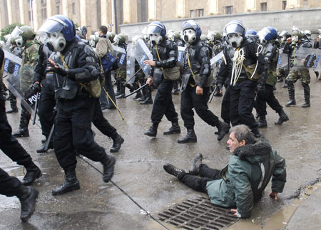 Police officers run by an opposition supporter sitting on the side of the road during a rally in front of the parliament building in Tbilisi Nov. 7, 2007. Georgian riot police fired rubber bullets, tear gas and water cannon on Wednesday to break up a six-day-old rally by protesters demanding the resignation of President Mikhail Saakashvili.